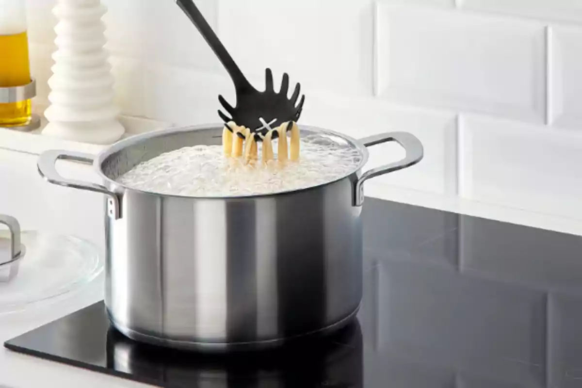 Olla de acero hirviendo agua con pasta y una cuchara de espagueti negra sosteniendo algunos macarrones Olla de acero hirviendo agua con pasta y una cuchara de espagueti negra sosteniendo algunos macarrones
