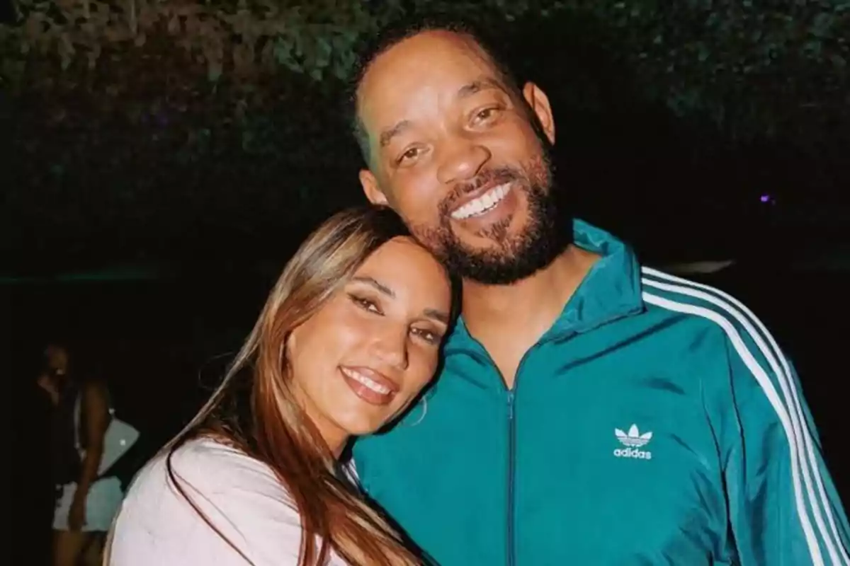 A couple smiles, hugging each other as they pose for a photo in a dimly lit setting. A couple smiles, hugging each other as they pose for a photo in a dimly lit setting.