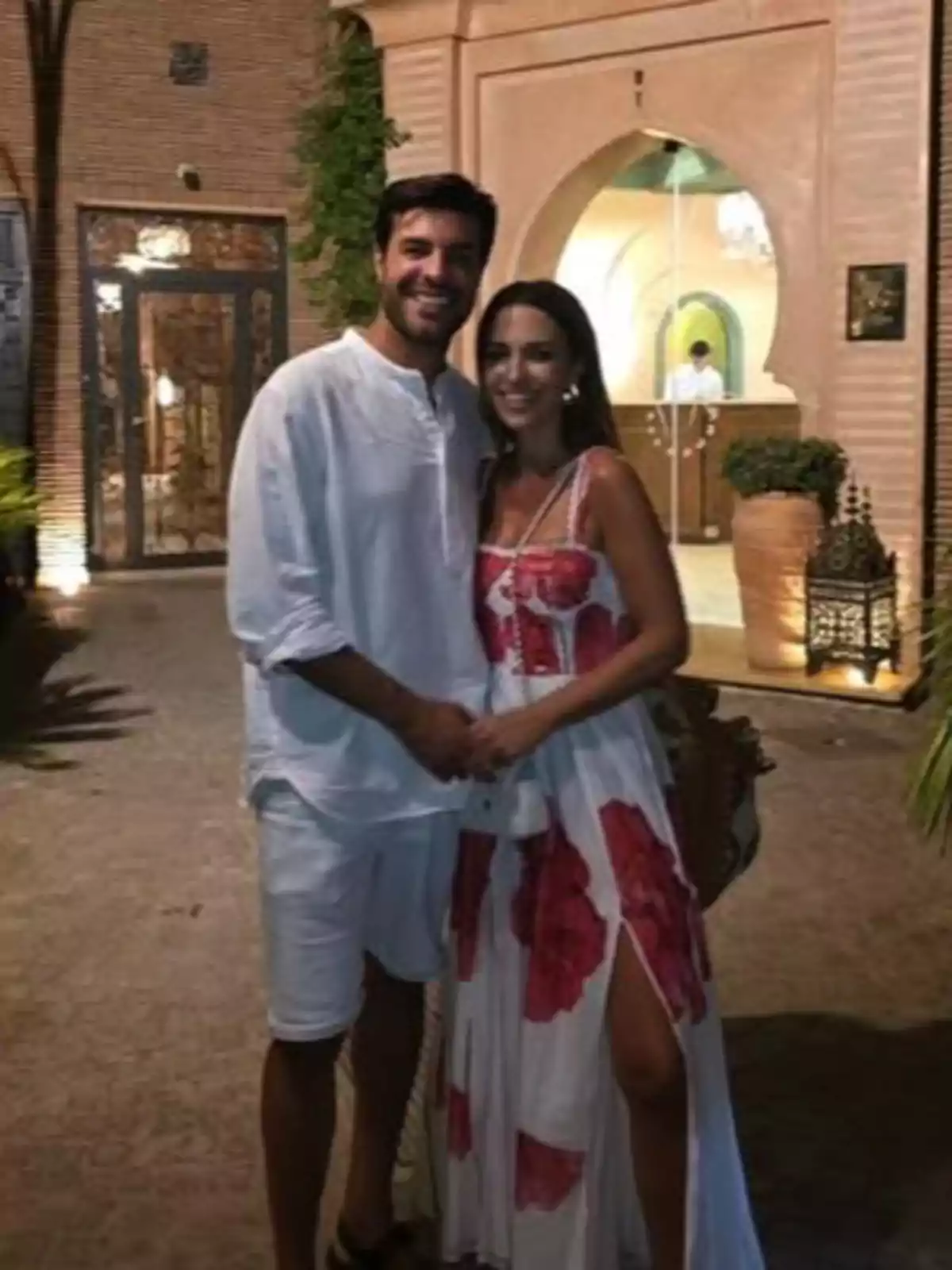 Paula Echevarría y Miguel Torres sonrientes posan abrazados al aire libre frente a una entrada decorada con arcos y plantas, ambos vestidos con ropa veraniega clara Paula Echevarría y Miguel Torres sonrientes posan abrazados al aire libre frente a una entrada decorada con arcos y plantas, ambos vestidos con ropa veraniega clara