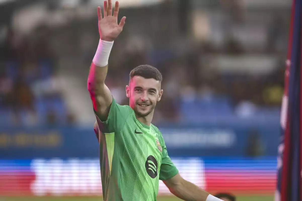 Portero de fútbol con uniforme verde saludando y sonriendo en un estadio