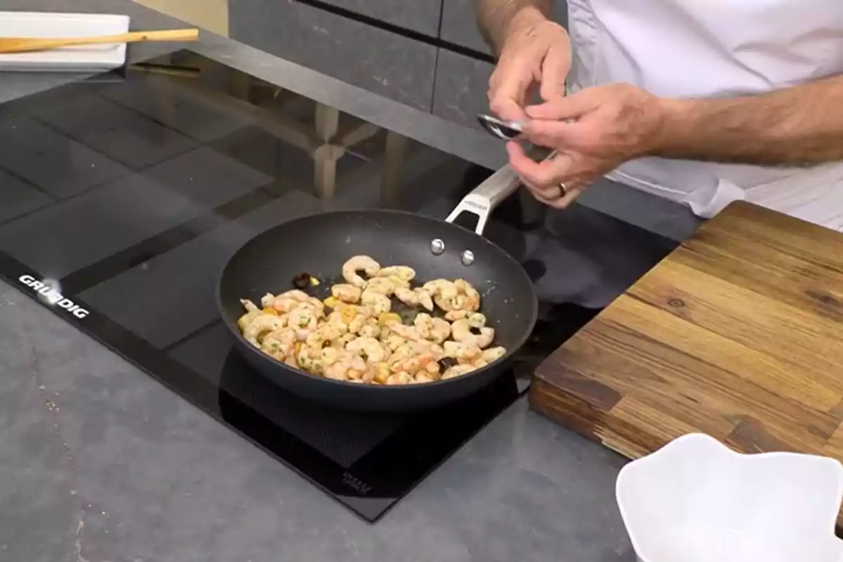 Karlos Arguiñano cuinant gambes en una paella sobre una cuina d’inducció al costat d’una taula de fusta i un recipient blanc Karlos Arguiñano cuinant gambes en una paella sobre una cuina d’inducció al costat d’una taula de fusta i un recipient blanc