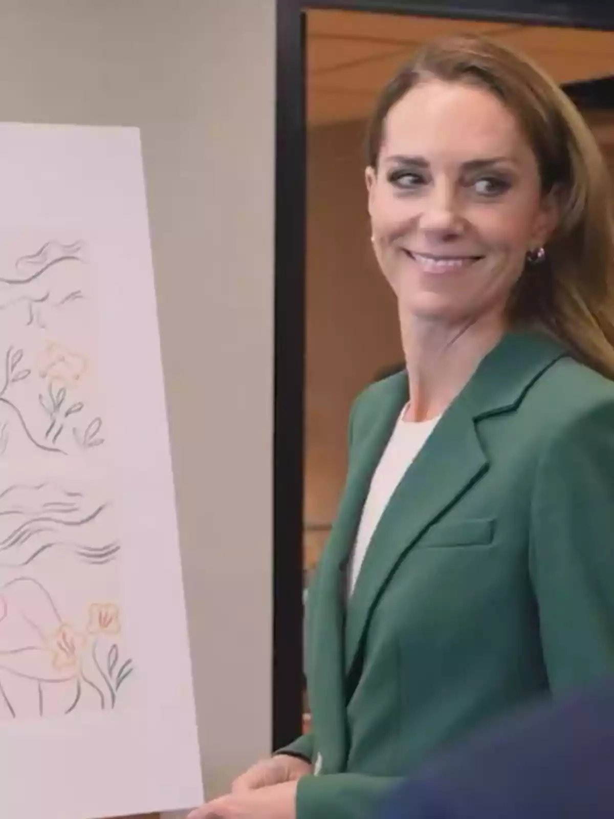 Mujer con saco verde sonriendo junto a una ilustración en un caballete Mujer con saco verde sonriendo junto a una ilustración en un caballete