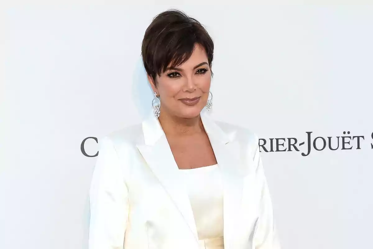 Kris Jenner amb un elegant vestit blanc i arracades llargues posant davant d’un fons clar Kris Jenner amb un elegant vestit blanc i arracades llargues posant davant d’un fons clar