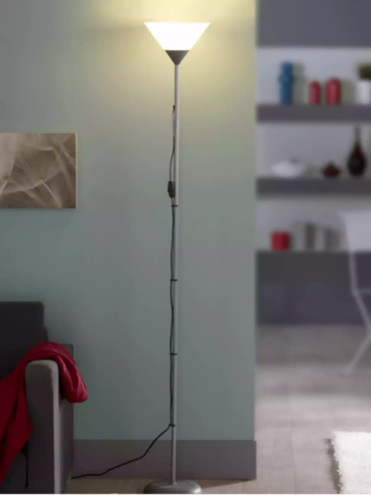 Làmpada de peu encesa al costat d’un sofà gris amb una manta vermella en una sala moderna Làmpada de peu encesa al costat d’un sofà gris amb una manta vermella en una sala moderna