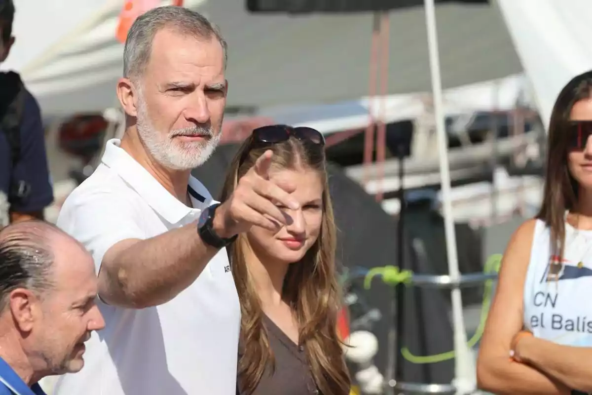 Un home de barba canosa assenyala cap endavant mentre està acompanyat de diverses persones en un ambient a l’aire lliure amb vaixells de fons. Un home de barba canosa assenyala cap endavant mentre està acompanyat de diverses persones en un ambient a l’aire lliure amb vaixells de fons.