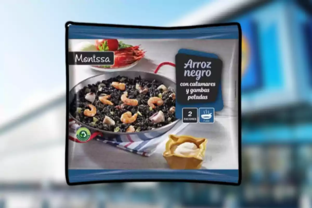 Paquet d’arròs negre amb calamars i gambes pelades de la marca Monissa mostrant una paella amb el plat preparat i una petita porció de salsa al costat Paquet d’arròs negre amb calamars i gambes pelades de la marca Monissa mostrant una paella amb el plat preparat i una petita porció de salsa al costat