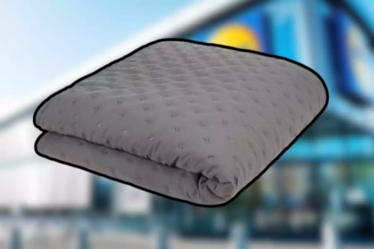 Manta grisa plegada amb textura encoixinada sobre un fons desenfocat d’una botiga Manta grisa plegada amb textura encoixinada sobre un fons desenfocat d’una botiga