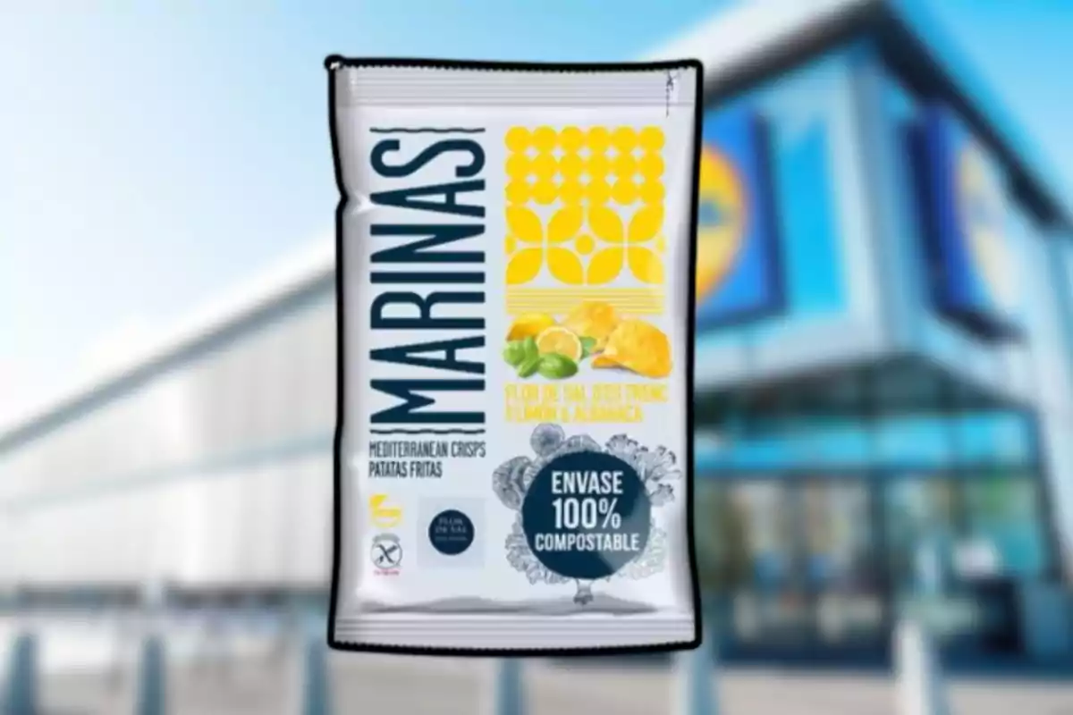Bossa de patates fregides Marines amb gust de llimona i alfàbrega, envàs 100% compostable, davant d’una botiga amb façana blava i groga desenfocada.