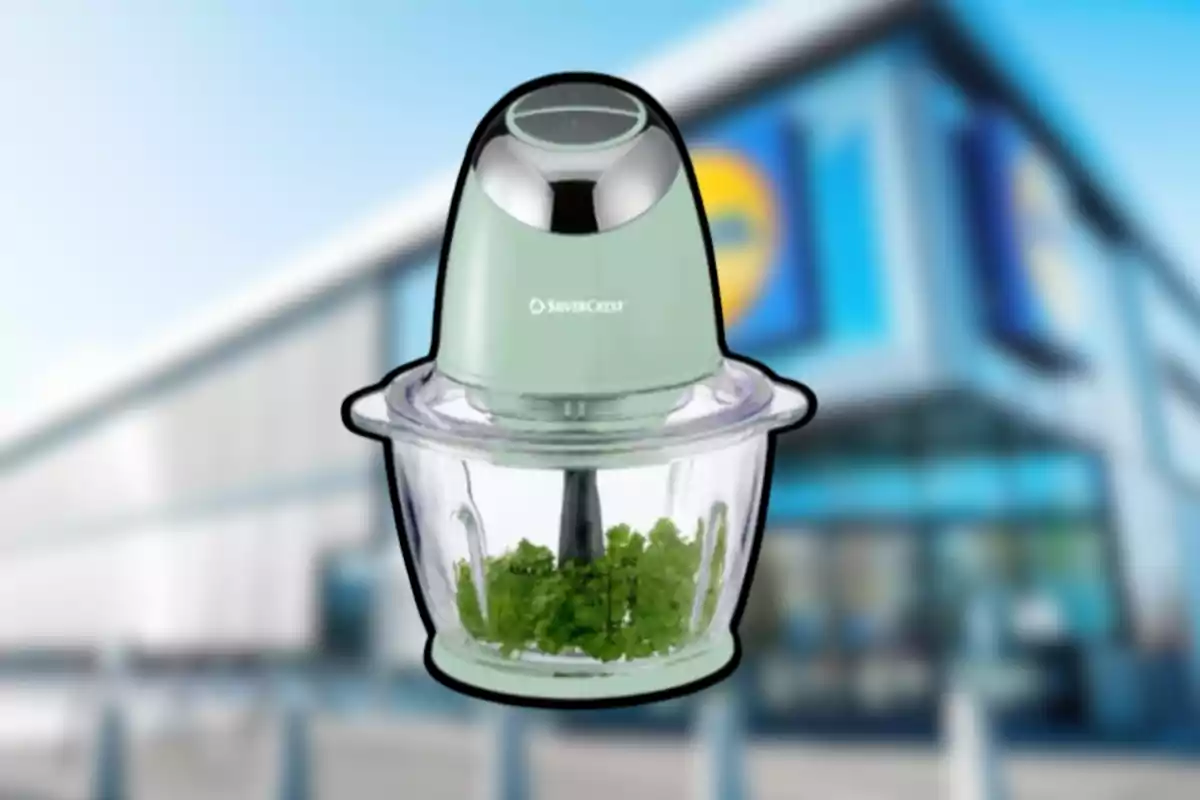 Processador d’aliments SilverCrest de color verd amb recipient de vidre i verdures picades a l’interior davant d’una botiga desenfocada Processador d’aliments SilverCrest de color verd amb recipient de vidre i verdures picades a l’interior davant d’una botiga desenfocada