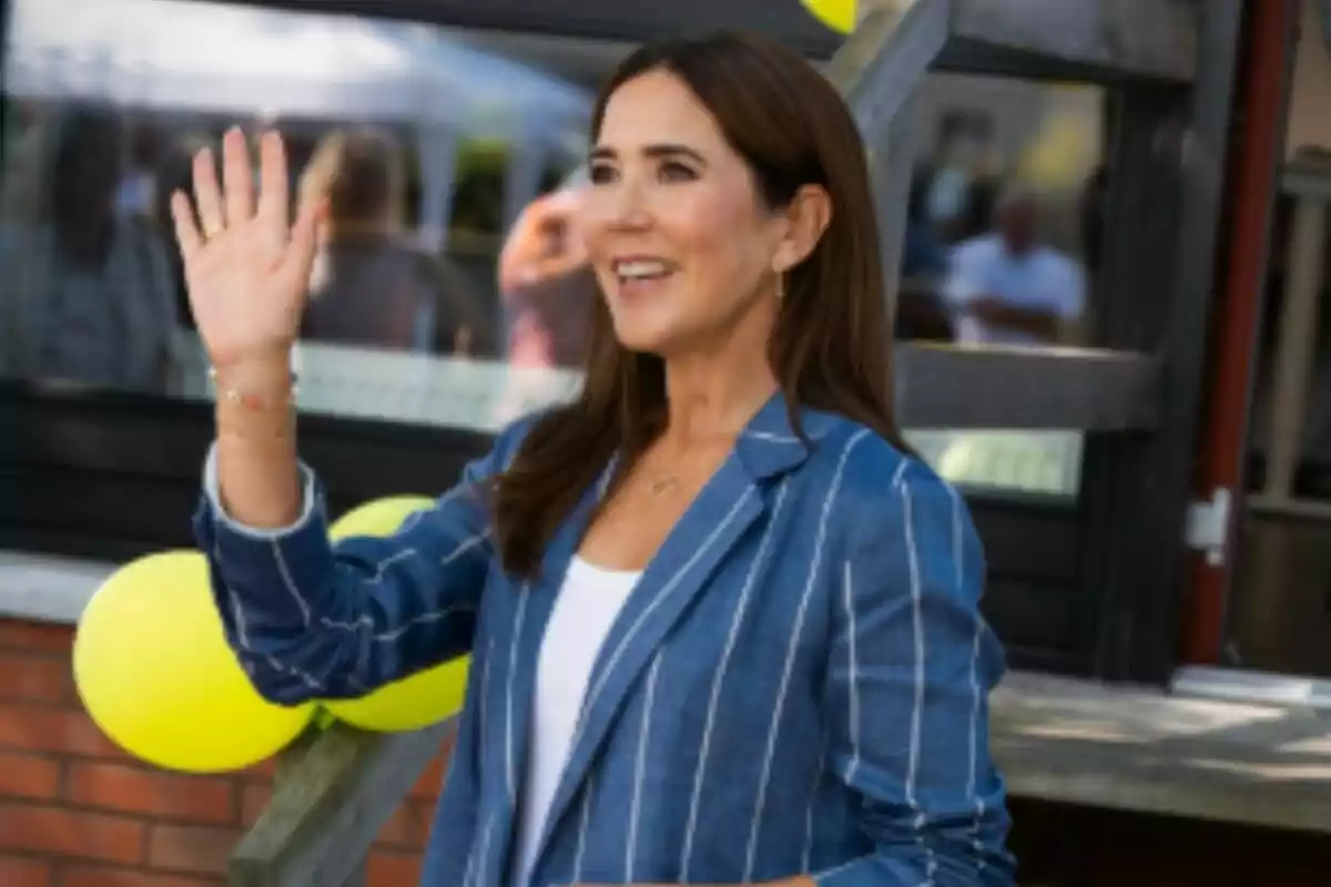 Pla mitjà de la reina María de Dinamarca somrient amb jaqueta blava de ratlles saludant amb la mà aixecada davant de globus grocs. Pla mitjà de la reina María de Dinamarca somrient amb jaqueta blava de ratlles saludant amb la mà aixecada davant de globus grocs.