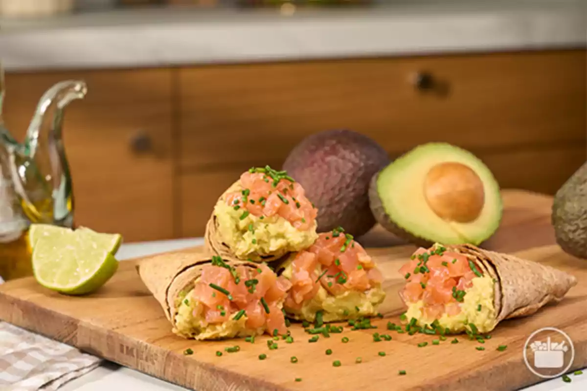 Conus de truita farcits de guacamole i salmó picat decorats amb cibulet sobre una taula de fusta amb alvocat i llima al fons Conus de truita farcits de guacamole i salmó picat decorats amb cibulet sobre una taula de fusta amb alvocat i llima al fons