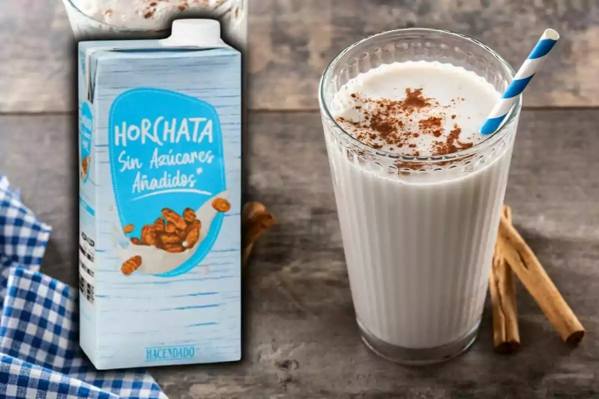 Vaso de horchata con canela en polvo y pajilla azul junto a un cartón de horchata sin azúcares añadidos sobre una mesa de madera. Vaso de horchata con canela en polvo y pajilla azul junto a un cartón de horchata sin azúcares añadidos sobre una mesa de madera.