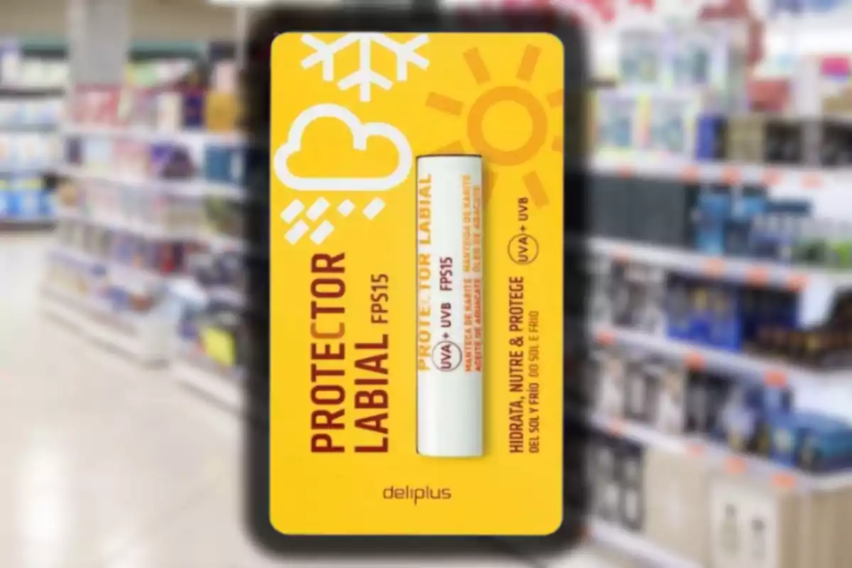 Protector labial Deliplus FPS 15 en el seu embolcall groc amb símbols de sol i neu, en un passadís de supermercat desenfocat.