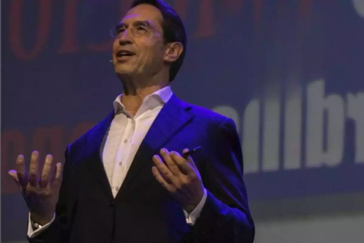 Home de mitjana edat amb ulleres i micròfon de diadema donant una conferència en un escenari il·luminat amb llum blava Home de mitjana edat amb ulleres i micròfon de diadema donant una conferència en un escenari il·luminat amb llum blava