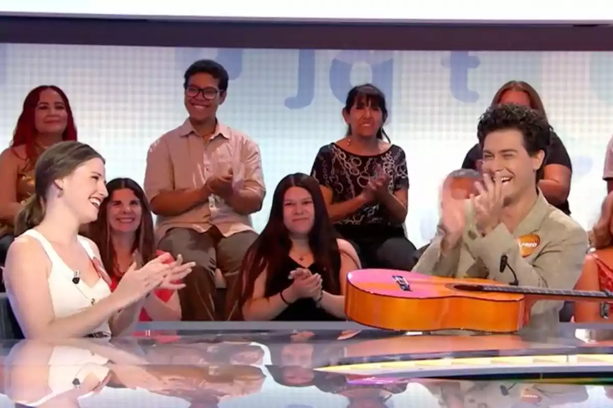 Isabel Moreno i Alfred Garcia somriuen i aplaudeixen en un programa de televisió mentre una guitarra descansa sobre la taula i el públic els observa i també aplaudeix. Captura de 'Pasapalabra' Isabel Moreno i Alfred Garcia somriuen i aplaudeixen en un programa de televisió mentre una guitarra descansa sobre la taula i el públic els observa i també aplaudeix. Captura de 'Pasapalabra'