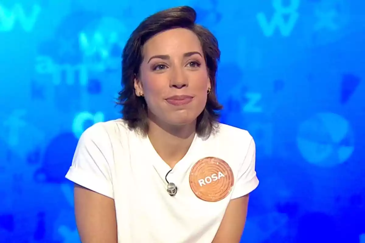 Rosa amb samarreta blanca i una etiqueta que diu Rosa sobre un fons blau amb lletres difuminades. Captura de 'Pasapalabra' Rosa amb samarreta blanca i una etiqueta que diu Rosa sobre un fons blau amb lletres difuminades. Captura de 'Pasapalabra'