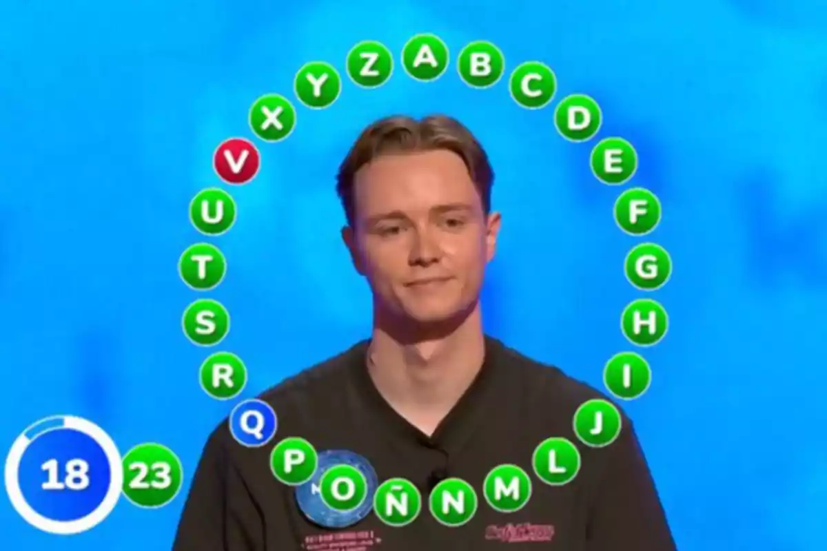 Manu està dret davant d’una pantalla blava amb lletres de l’abecedari en cercle i un temporitzador a la cantonada inferior esquerra que mostra 18 segons. Captura de ‘Pasapalabra’