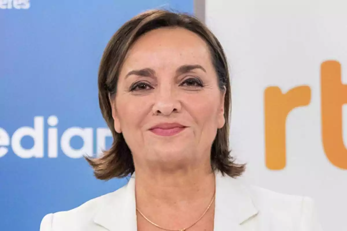 Pepa Bueno de mediana edad con cabello corto y castaño, vestida con chaqueta blanca y fondo con logotipos azules y naranjas del Telediario. Pepa Bueno de mediana edad con cabello corto y castaño, vestida con chaqueta blanca y fondo con logotipos azules y naranjas del Telediario.