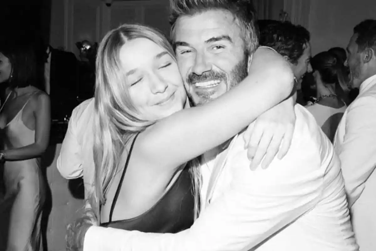Harper y David Beckham sonríen y se abrazan en una fiesta elegante mientras otras personas conversan al fondo Harper y David Beckham sonríen y se abrazan en una fiesta elegante mientras otras personas conversan al fondo