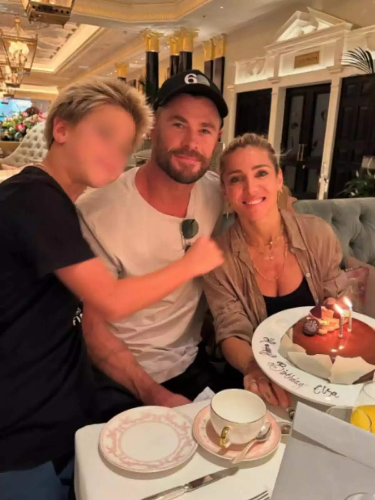 Una familia celebrando un cumpleaños en un elegante restaurante, con una mujer sosteniendo un pastel con velas y todos sonriendo hacia la cámara. Una familia celebrando un cumpleaños en un elegante restaurante, con una mujer sosteniendo un pastel con velas y todos sonriendo hacia la cámara.