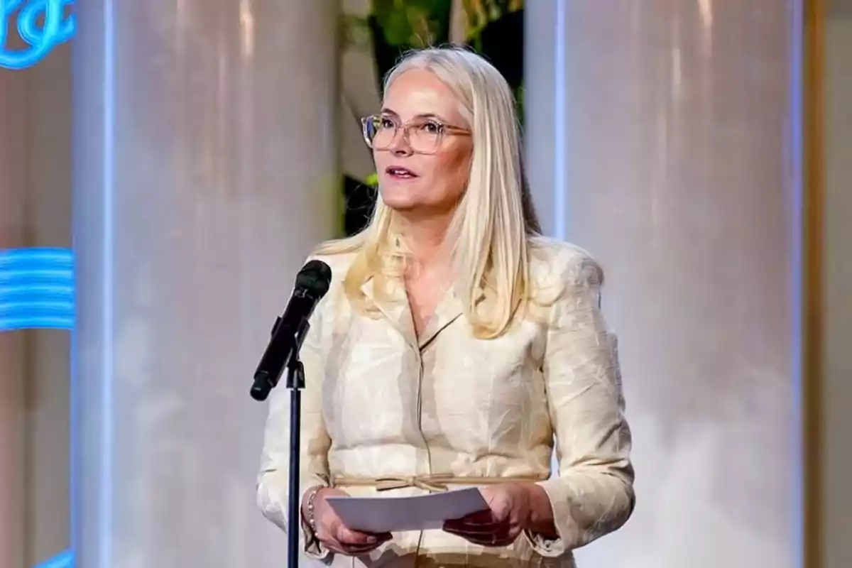 Mette-Marit amb ulleres parlant davant d’un micròfon mentre sosté uns fulls Mette-Marit amb ulleres parlant davant d’un micròfon mentre sosté uns fulls