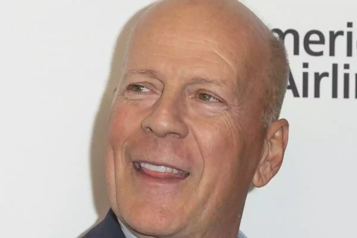 Bruce Willis somrient i mirant cap a un costat amb fons blanc i lletres negres parcialment visibles Bruce Willis somrient i mirant cap a un costat amb fons blanc i lletres negres parcialment visibles