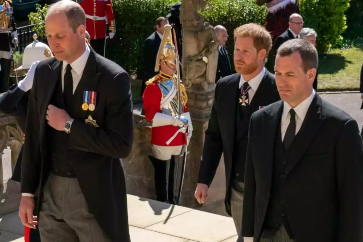 Princes William and Harry and Peter Phillips, dressed in formal suits, walk together at a solemn outdoor event while a guard in ceremonial uniform stands in the background. Princes William and Harry and Peter Phillips, dressed in formal suits, walk together at a solemn outdoor event while a guard in ceremonial uniform stands in the background.