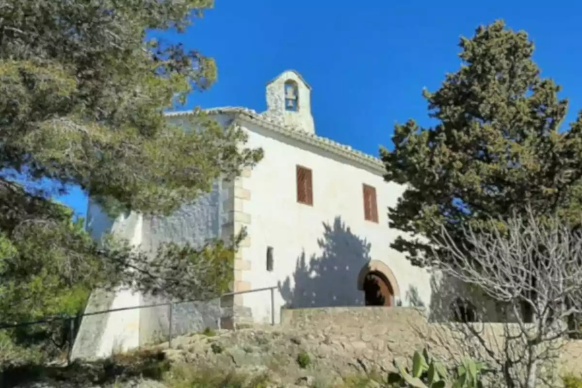 Ermita blanca rodeada de árboles bajo un cielo azul despejado Ermita blanca rodeada de árboles bajo un cielo azul despejado