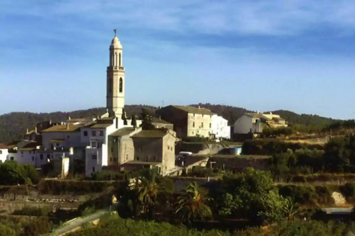 Poble rural amb cases de pedra i una església amb campanar envoltada de vegetació i turons sota un cel blau