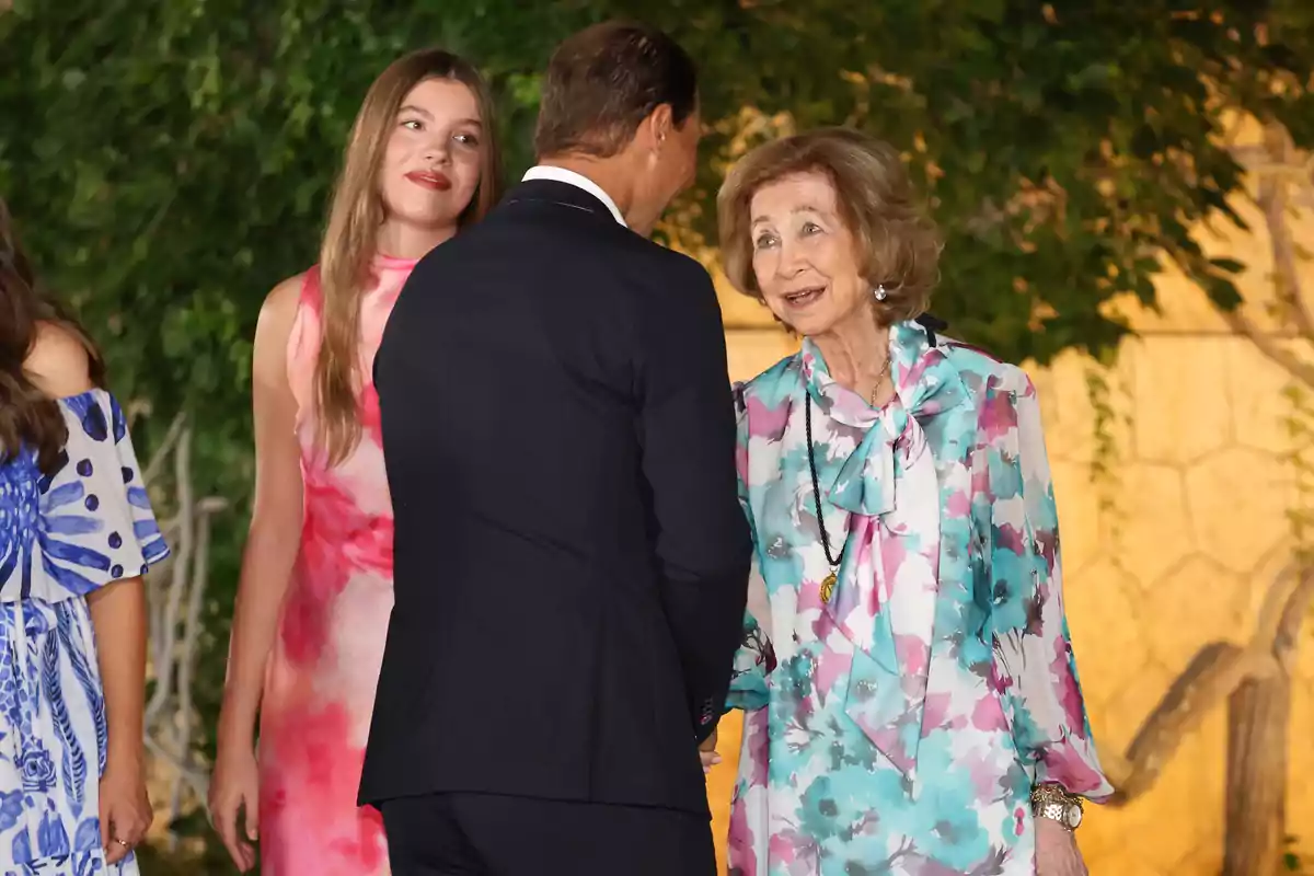 La infanta Sofia, Rafa Nadal i la reina Sofia elegantment vestides conversen a l’aire lliure durant un esdeveniment social. La infanta Sofia, Rafa Nadal i la reina Sofia elegantment vestides conversen a l’aire lliure durant un esdeveniment social.