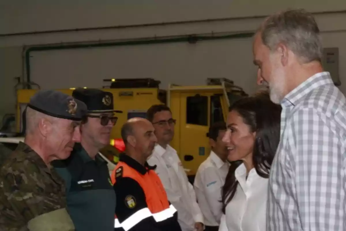 A group of people, including authorities and emergency personnel, are talking inside a building with vehicles in the background. A group of people, including authorities and emergency personnel, are talking inside a building with vehicles in the background.
