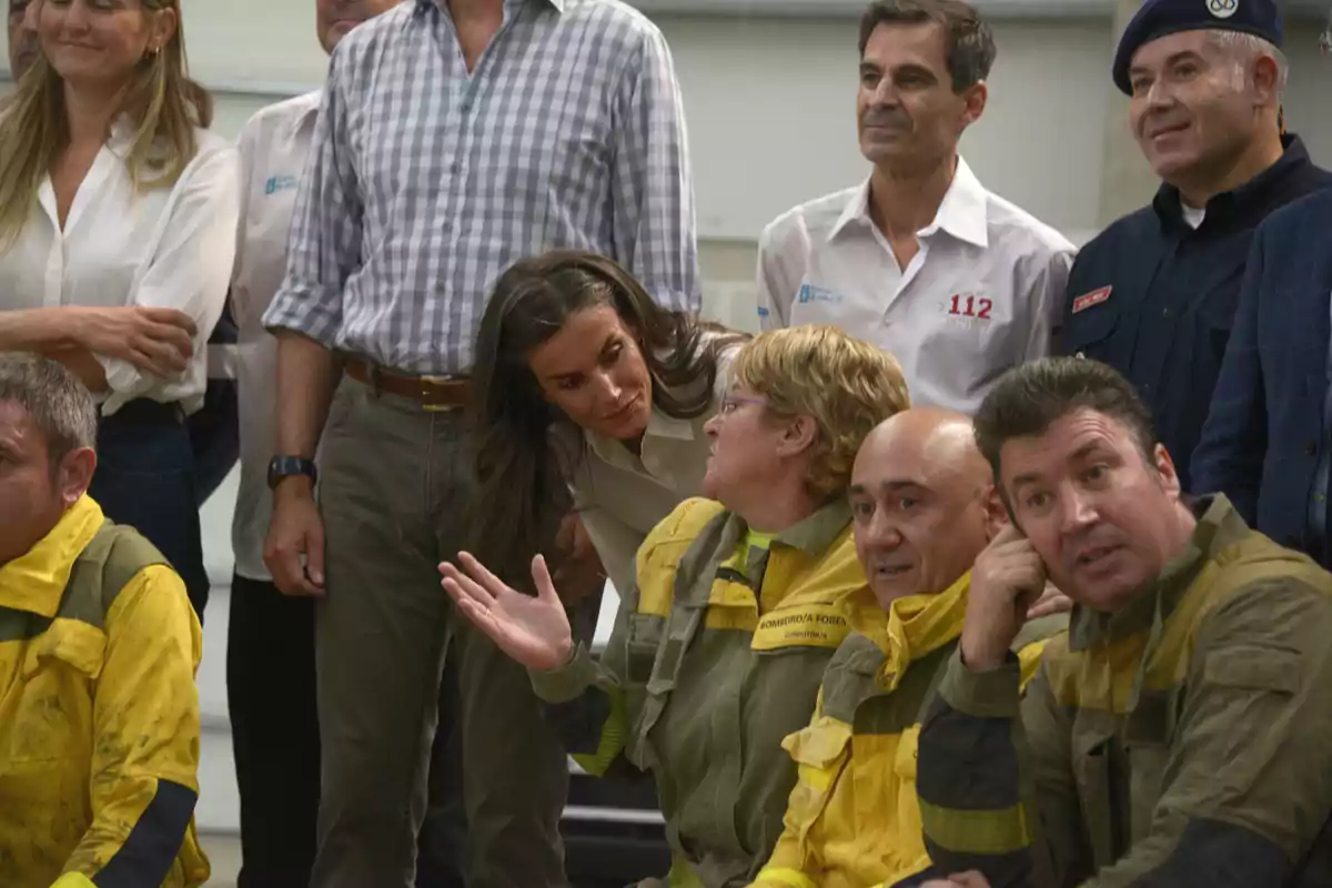 A group of people, including several wildland firefighters in yellow uniforms, are talking and smiling in an informal setting. A group of people, including several wildland firefighters in yellow uniforms, are talking and smiling in an informal setting.