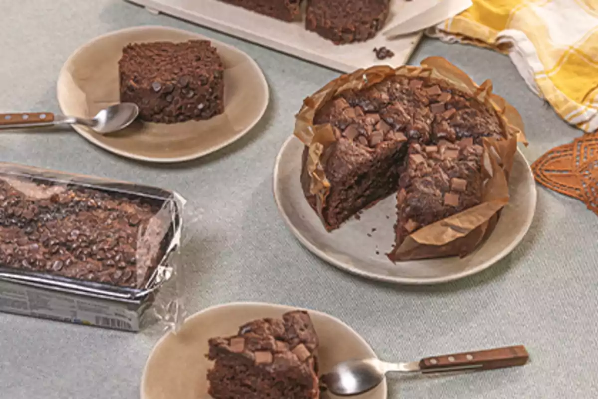 Diversos pastissos de xocolata servits en plats amb culleres sobre una taula, un d’ells en el seu envàs i un altre tallat a llesques. Diversos pastissos de xocolata servits en plats amb culleres sobre una taula, un d’ells en el seu envàs i un altre tallat a llesques.