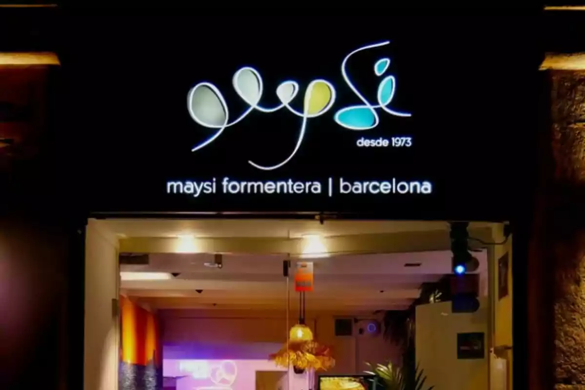 Entrada il·luminada d’un local amb un rètol que diu maysi formentera barcelona i un logotip colorit sobre fons negre Entrada il·luminada d’un local amb un rètol que diu maysi formentera barcelona i un logotip colorit sobre fons negre
