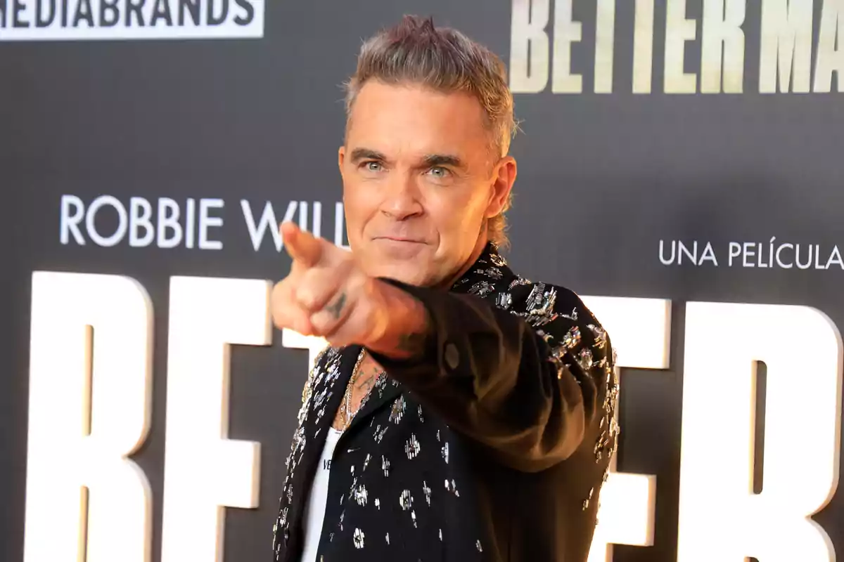 Robbie Williams pointing at the camera on a red carpet with a background of large, shiny letters Robbie Williams pointing at the camera on a red carpet with a background of large, shiny letters