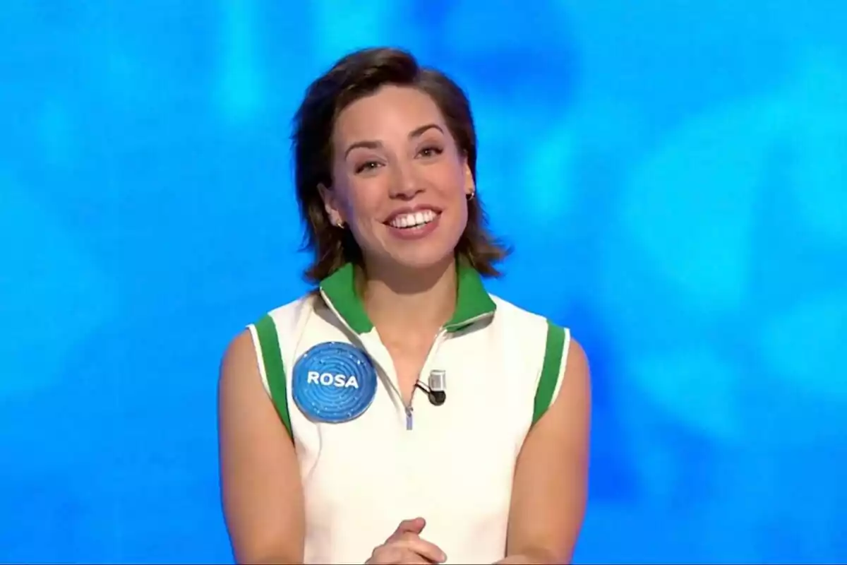 Rosa Rodríguez somrient amb cabell curt i fosc, vestida amb una samarreta de tirants blanca amb detalls verds i un gafet blau que diu Rosa, sobre un fons blau. Rosa Rodríguez somrient amb cabell curt i fosc, vestida amb una samarreta de tirants blanca amb detalls verds i un gafet blau que diu Rosa, sobre un fons blau.