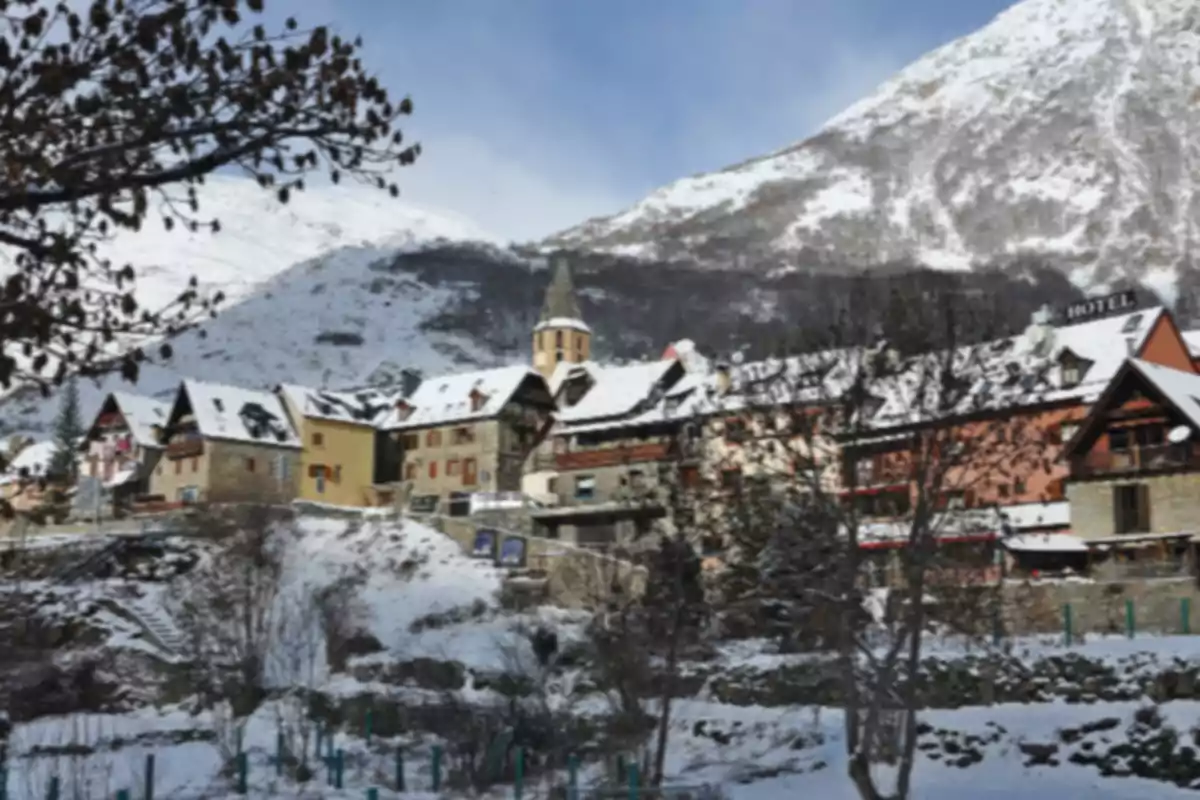 Pueblo de montaña con casas y tejados cubiertos de nieve rodeado de montañas nevadas en un día despejado