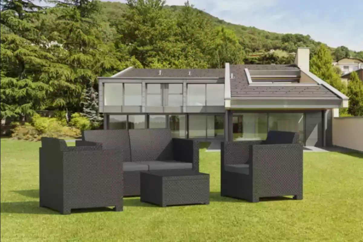 Conjunt de mobles de jardí de color fosc sobre gespa davant d’una casa moderna envoltada d’arbres i vegetació Conjunt de mobles de jardí de color fosc sobre gespa davant d’una casa moderna envoltada d’arbres i vegetació