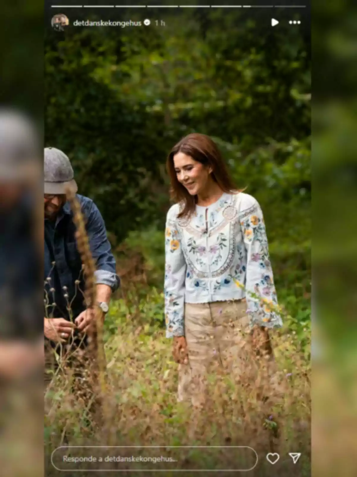 Mary de Dinamarca somrient amb una brusa brodada i una faldilla beix caminant per un camp envoltada de vegetació al costat d’un home parcialment visible Mary de Dinamarca somrient amb una brusa brodada i una faldilla beix caminant per un camp envoltada de vegetació al costat d’un home parcialment visible