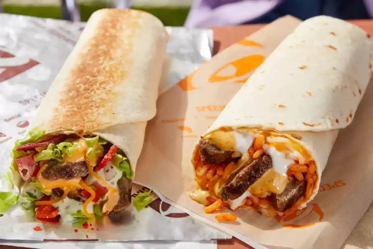 Dos burritos de tortilla de harina rellenos, uno con carne, lechuga, tomate y aderezo, y el otro con carne, arroz, queso y salsa cremosa, sobre envolturas de papel. Dos burritos de tortilla de harina rellenos, uno con carne, lechuga, tomate y aderezo, y el otro con carne, arroz, queso y salsa cremosa, sobre envolturas de papel.