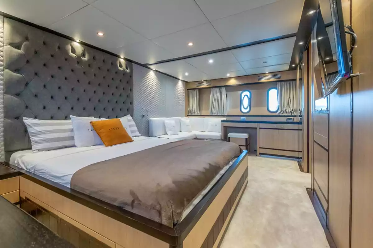 Habitació moderna i luxosa amb llit gran, capçalera entapissada, sofà blanc, escriptori, finestres rodones i decoració en tons neutres del iot Lefty Habitació moderna i luxosa amb llit gran, capçalera entapissada, sofà blanc, escriptori, finestres rodones i decoració en tons neutres del iot Lefty