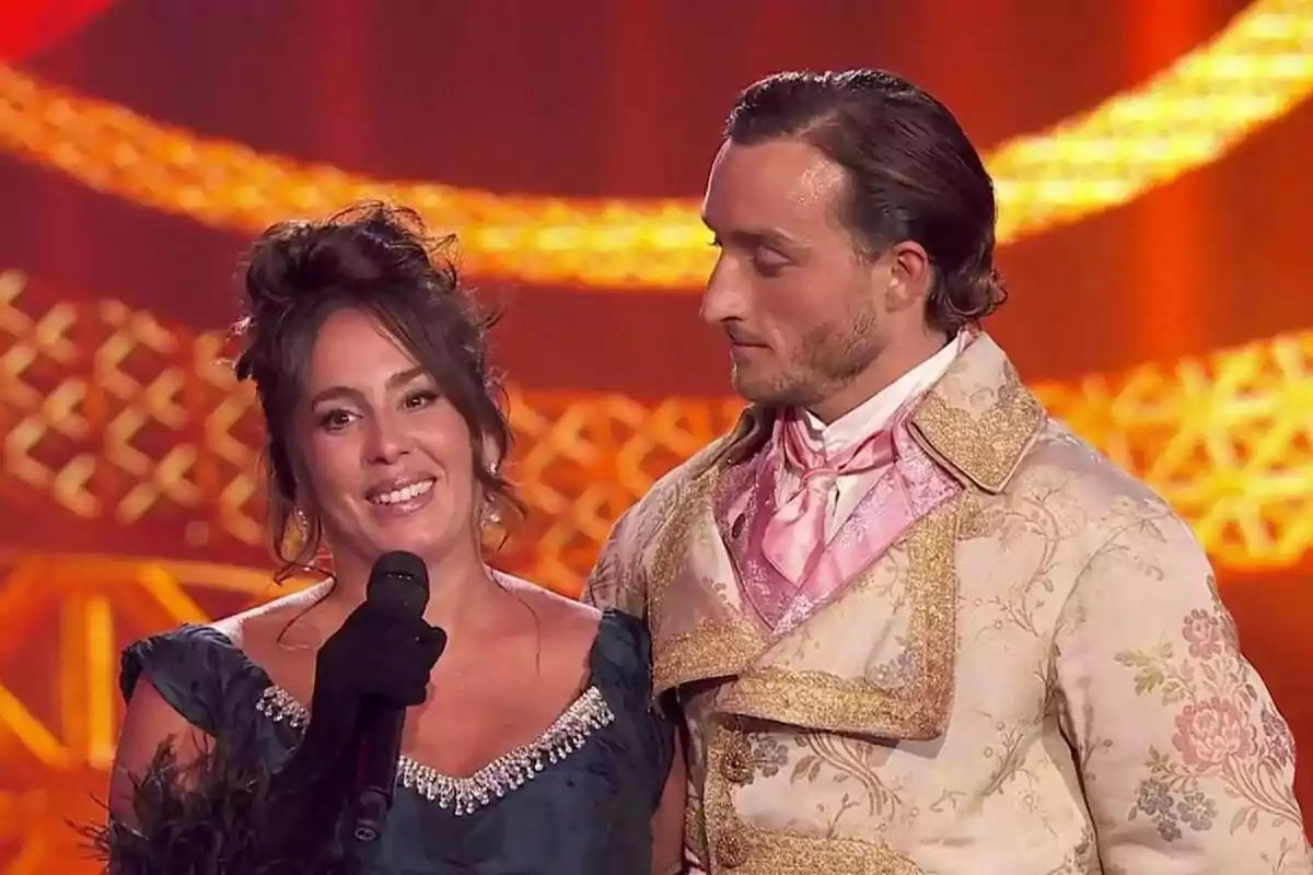Dues persones amb vestimenta d’època posen en un escenari il·luminat, Anabel Pantoja sosté un micròfon i somriu mentre l’altra la mira a Bailando con las estrellas.
