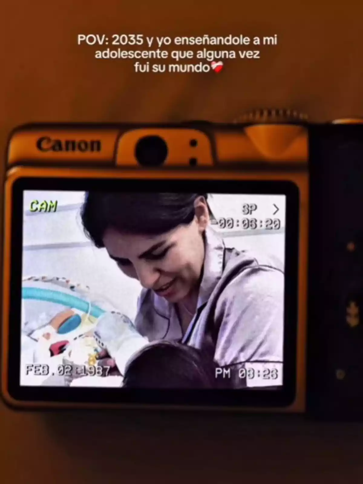 Una cámara muestra en su pantalla la imagen de Isa Pantoja sonriendo y mirando a su bebé mientras sostiene su manita, con un texto en la parte superior que habla sobre recordar el pasado con su hijo adolescente en el año 2035.