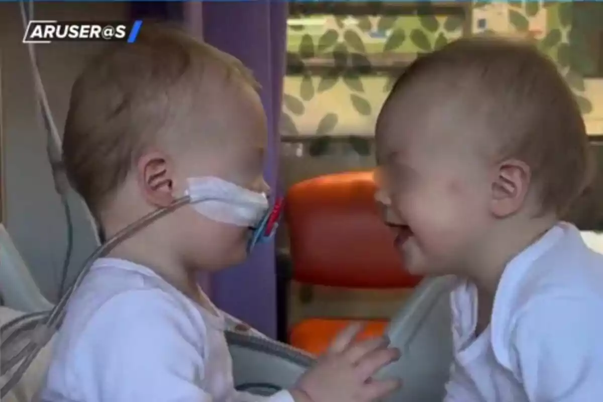 Dos nadons petits es miren i somriuen, un d’ells porta una sonda nasal i tots dos van vestits amb roba blanca en un entorn hospitalari.