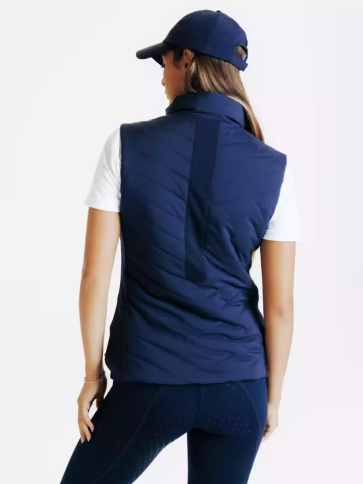 Dona d’esquena amb armilla blau marí, samarreta blanca, malles i gorra blau marí