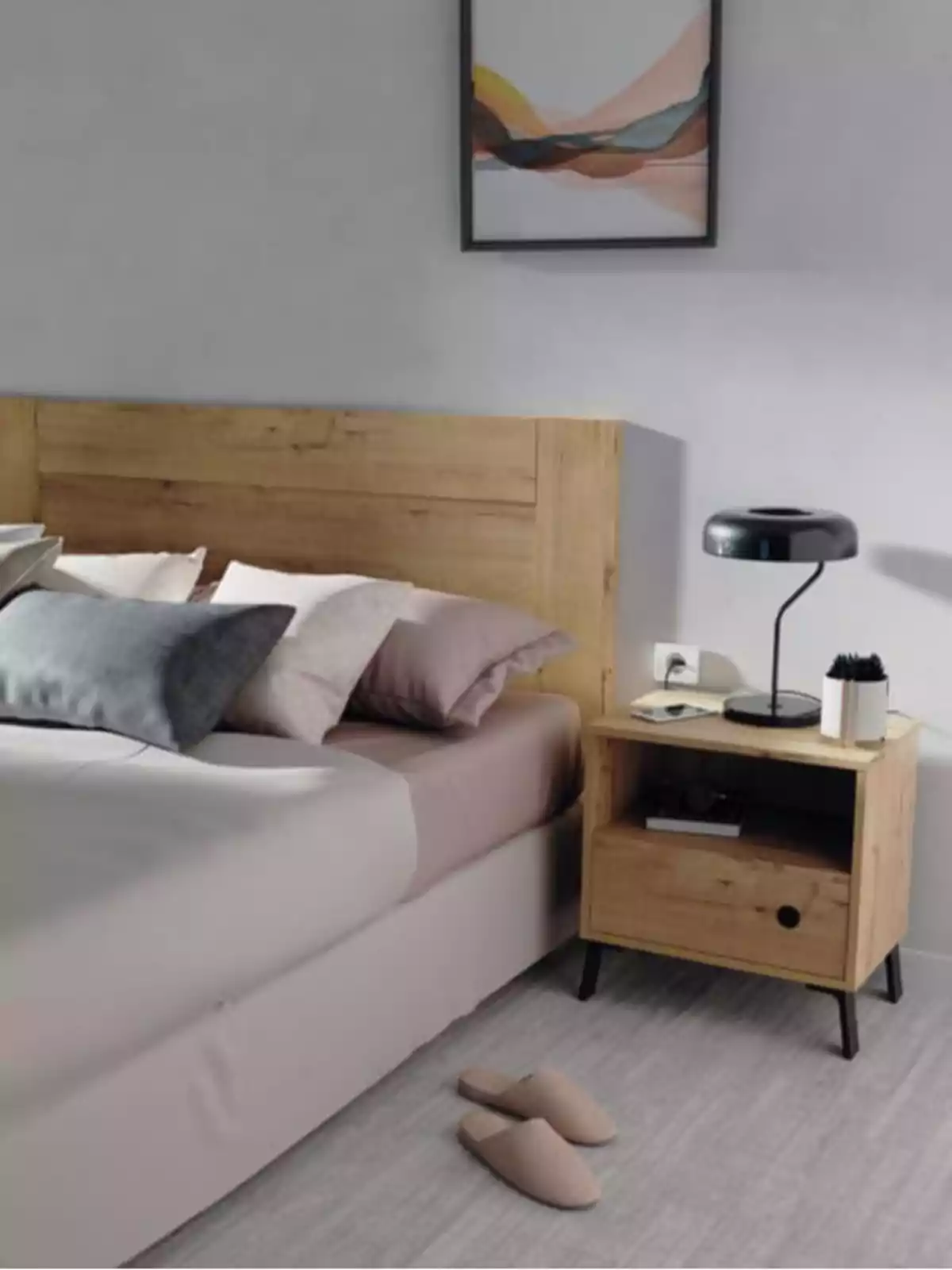 Habitació moderna amb llit de fusta, tauleta de nit, làmpada negra, sabatilles beix a terra i un quadre abstracte a la paret.