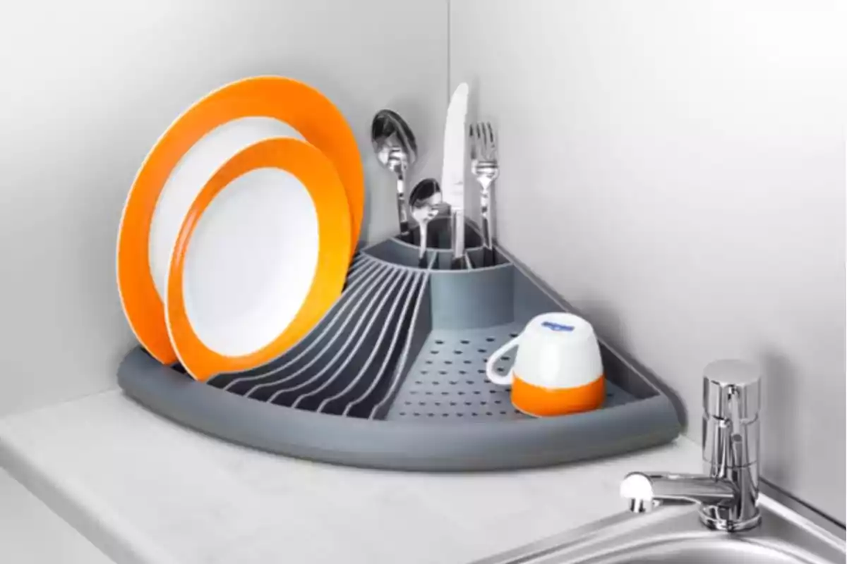 Escorreplats d’angle de color gris amb plats, coberts i una tassa al costat d’una pica moderna Escorreplats d’angle de color gris amb plats, coberts i una tassa al costat d’una pica moderna