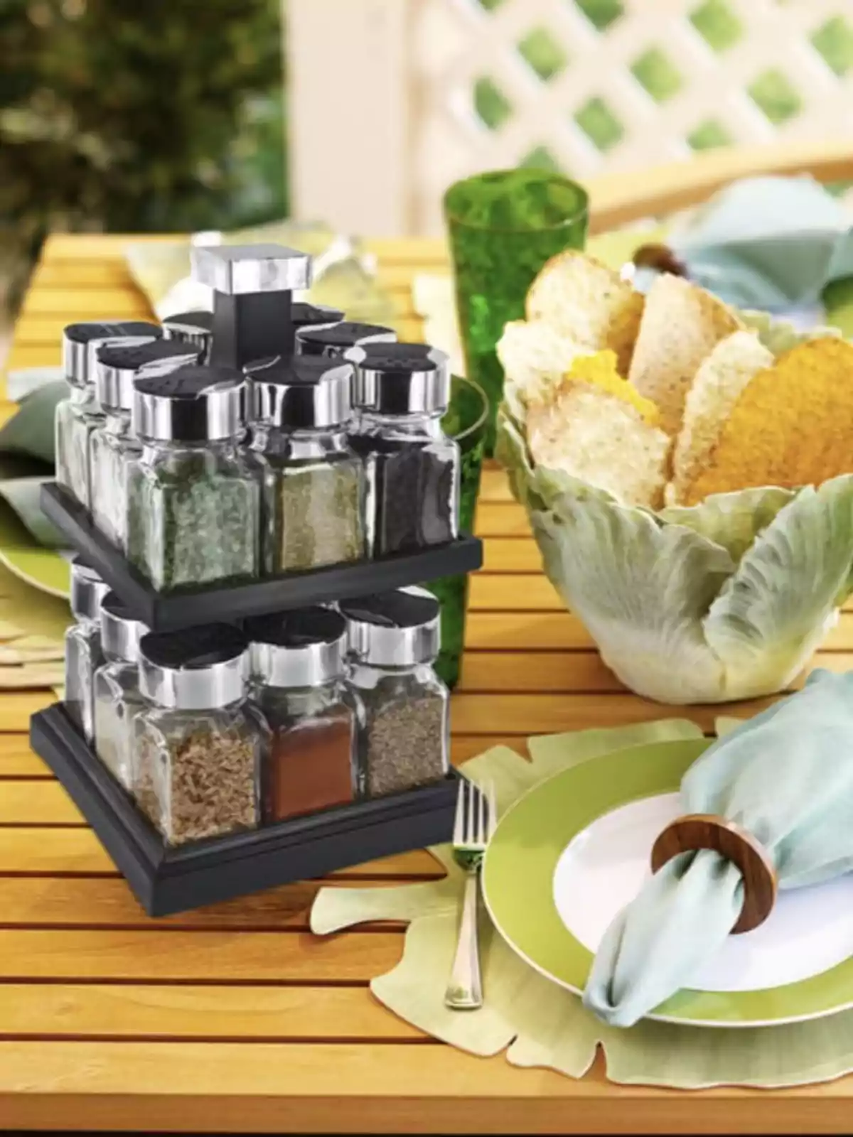 Un organitzador d'espècies amb pots de vidre sobre una taula de fusta a l'aire lliure al costat d'un plat amb tovalló i un bol amb llesques de pa