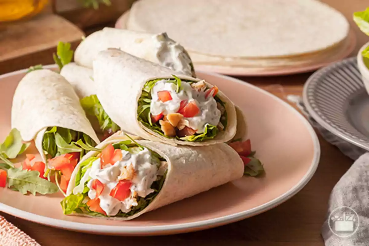 Tres wraps de truita farcits de pollastre, enciam, tomàquet i salsa cremosa servits en un plat rosa