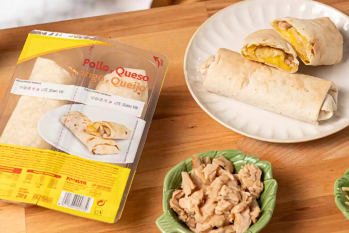 Burritos de pollastre i formatge en un plat al costat del seu embolcall i un recipient amb trossos de pollastre sobre una taula de fusta Burritos de pollastre i formatge en un plat al costat del seu embolcall i un recipient amb trossos de pollastre sobre una taula de fusta
